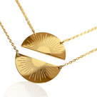 Two gold duo necklace pendants, one with rays resembling a sunrise and the other with a sunset glow, on a gold chain.