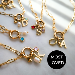 A collection of gold-plated necklaces with various charms, including letter charms, birthstones, and other thematic charms like hearts and moons.